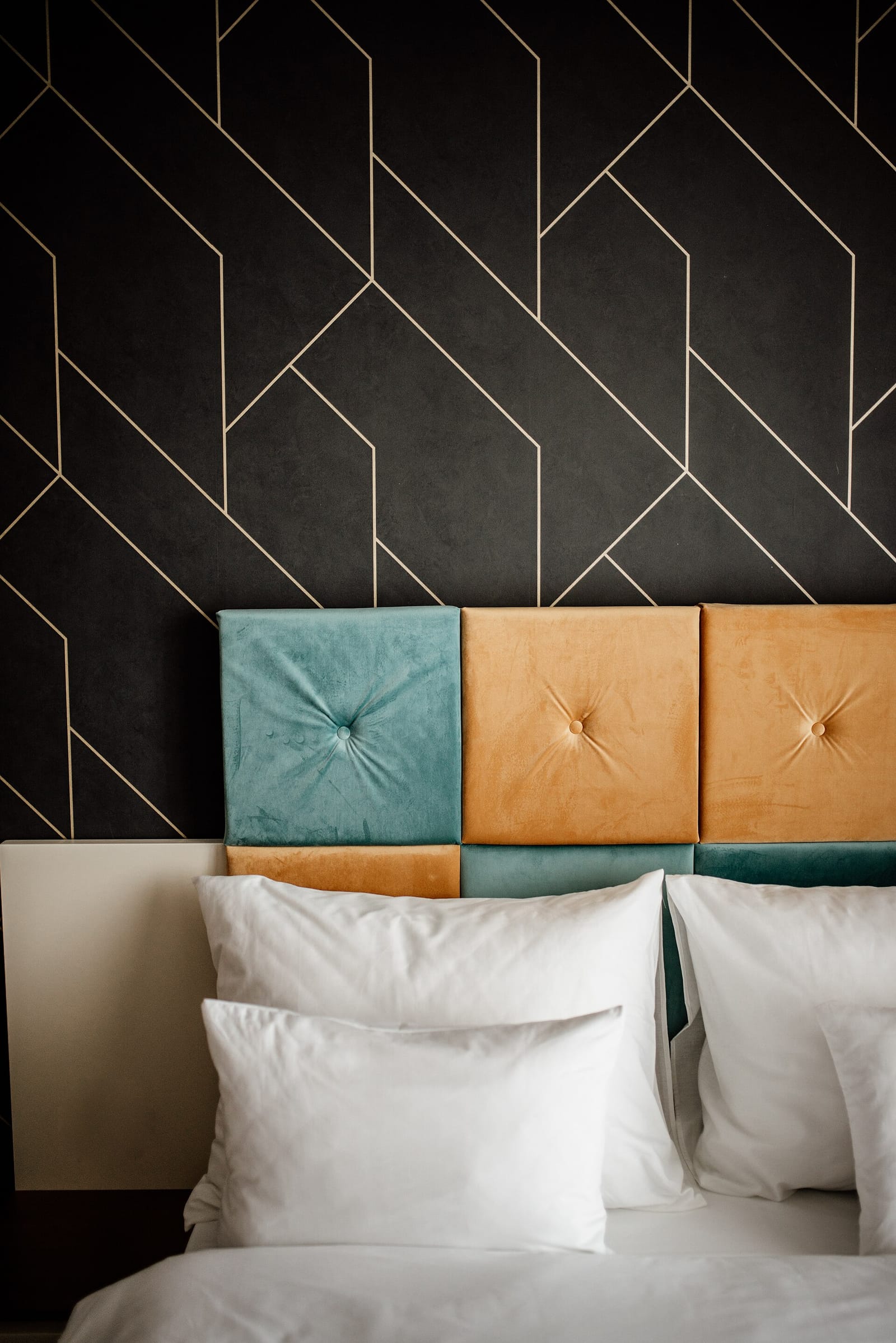 Crisp white pillows and folded bed linen against a dark patterned headboard wall.
